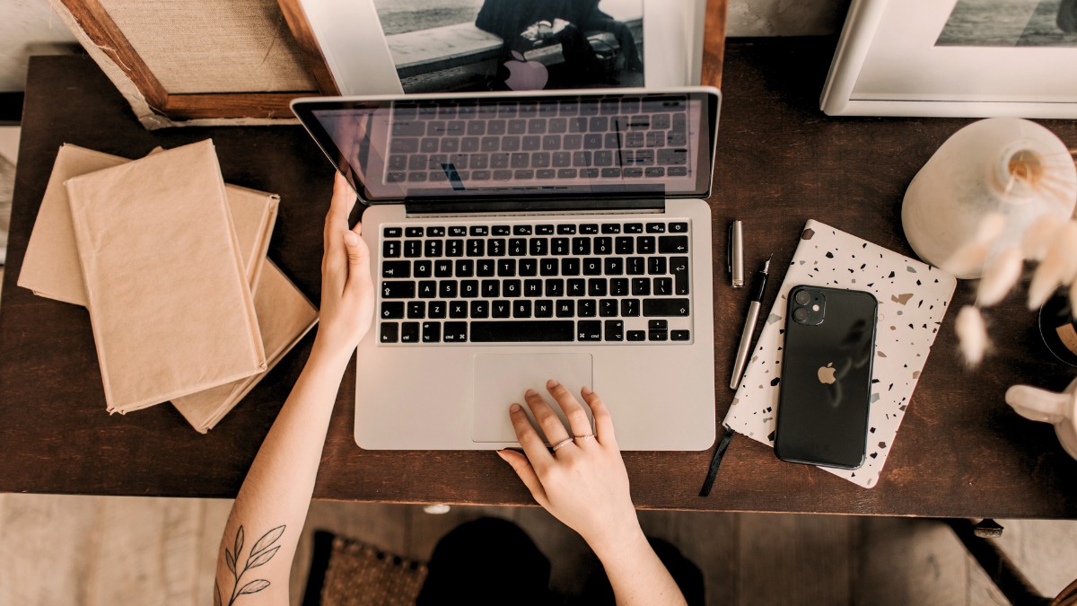 Notebook em cima de mesa rústica e mão de mulher criando conteúdo para blog de startup
